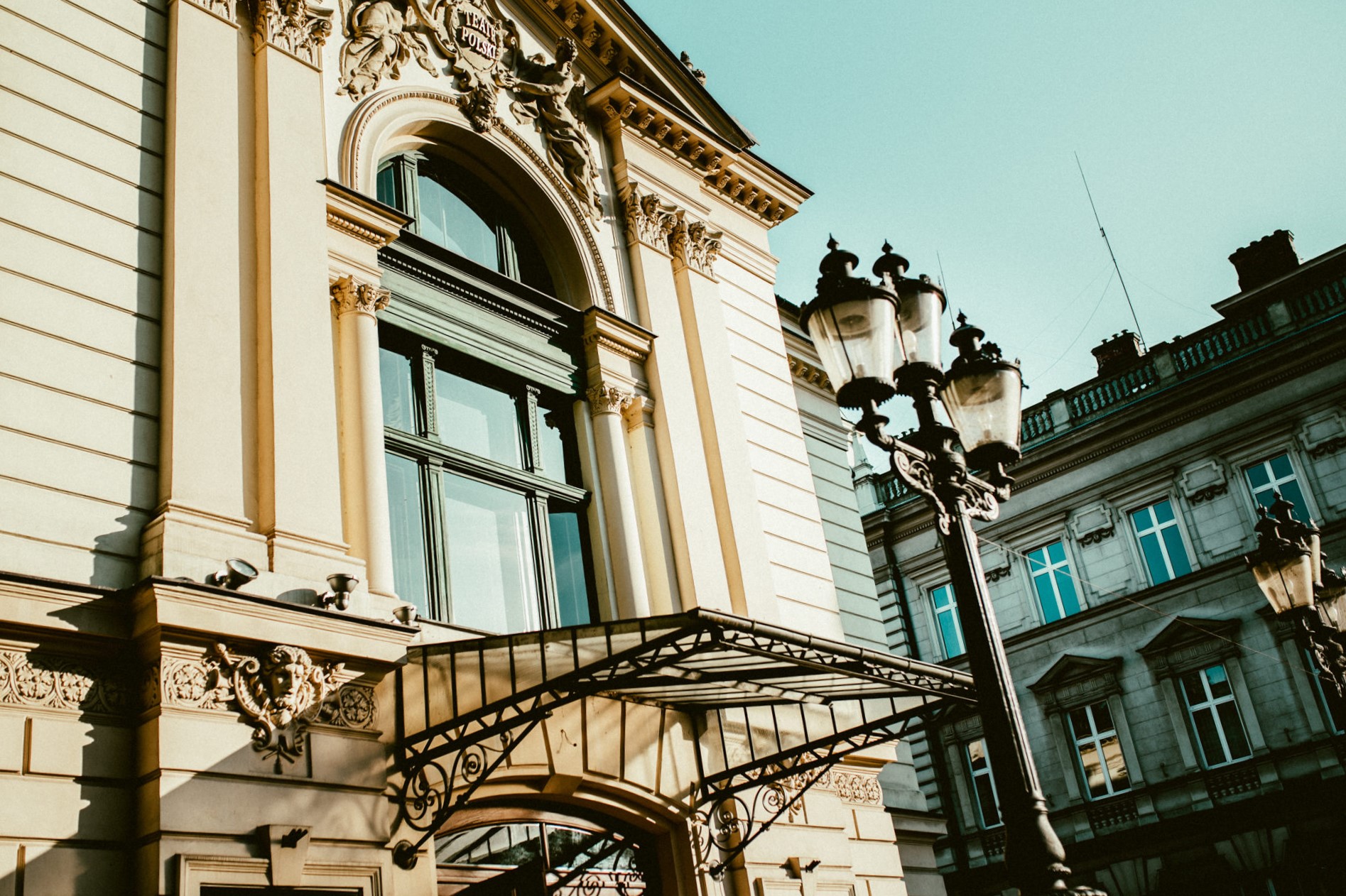 Fragment fasady zabytkowego budynku Teatru Polskiego, z dużym, półokrągłym oknem nad wejściem głównym. 