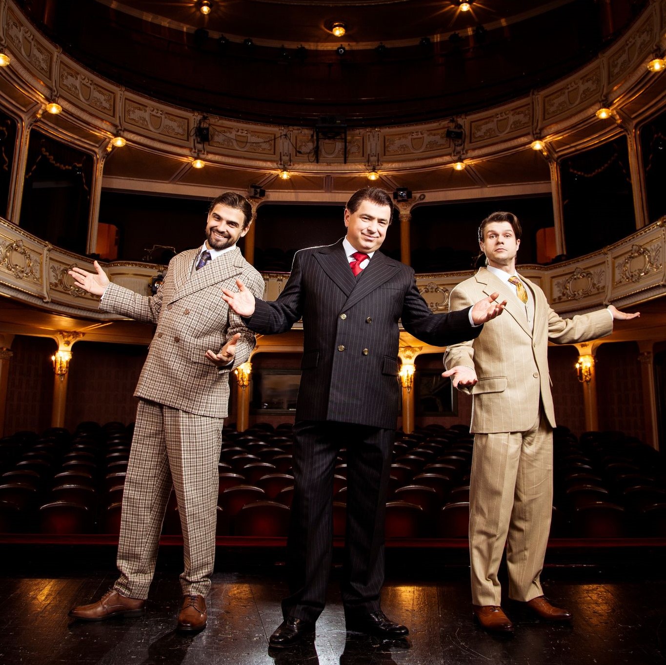Na scenie stoi trzech aktorów. Wszyscy uśmiechnięci, ubrani w garnitury. 