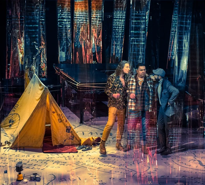 Na zdjęciu, na scenie teatru stoi trzech mężczyzn w średnim wieku. Obok nich stoi mały żółty namiot.