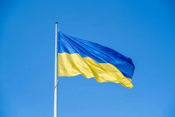 Na zdjęciu ukraińska flaga w niebiesko-żółtych barwach powiewa na tle błękitnego nieba. 