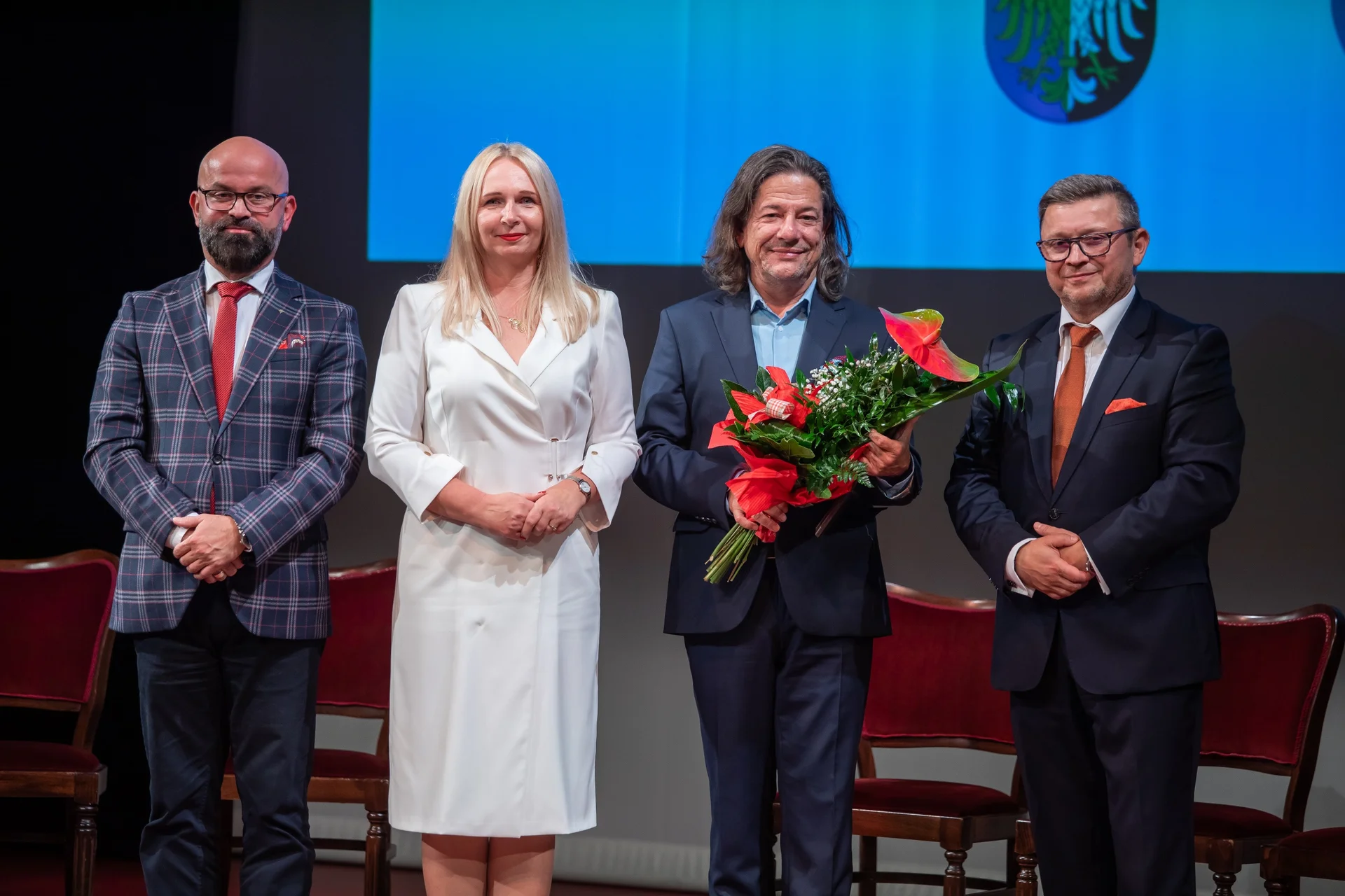  Cztery osoby stoją na scenie, wśród nich Witold Mazurkiewicz - dyrektor teatru z bukietem kwiatów. 